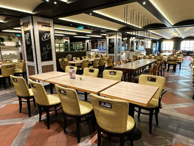 The main dining room on the Costa Smeralda cruise ship, featuring elegant wooden tables and chairs, decorative lighting, and a welcoming, spacious layout ready to host guests for a meal.