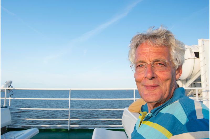 An older man in a striped shirt enjoying the ocean view from the deck of a cruise ship, with a relaxed and content expression.