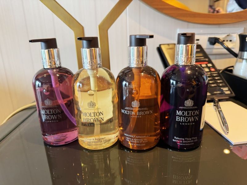 A collection of Molton Brown toiletries provided on the Seabourn Venture, adding a touch of luxury to the guests' experience. The selection includes four elegantly designed bottles: Relaxing Ylang-Ylang, Heavenly Gingerlily, Orange & Bergamot, and Blossoming Honeysuckle & White Tea bath and shower gels. These premium products are known for their delightful fragrances and quality ingredients, enhancing the pampering experience aboard the ship. Displayed on a sleek surface, these toiletries reflect the ship's commitment to offering high-end amenities to its guests.