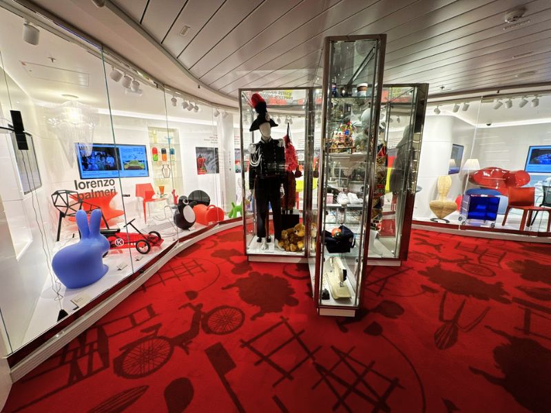 Interior of a museum on Costa Smeralda, showcasing a collection of modern art and design items, including vibrant furniture and eclectic decorations, set against a bold red carpet with patterned accents.