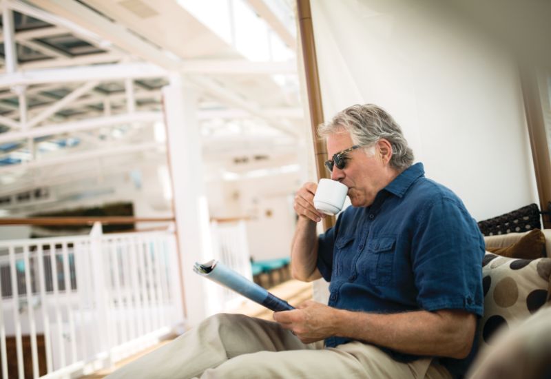 An old man on NCL cruise ship relaxing through a cup of coffee and a magazine 