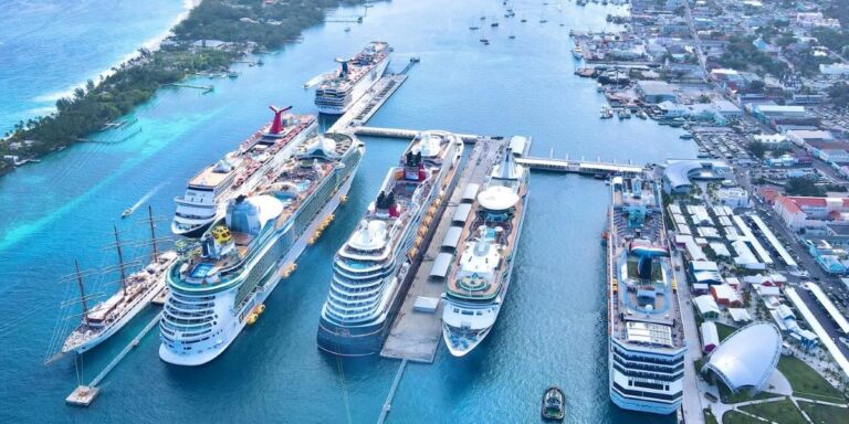 This image features Nassau Cruise Port bustling with activity, showing seven cruise ships docked side by side along the pier. The turquoise waters contrast with the urban backdrop, and the port area includes various buildings, infrastructure, and recreational areas, illustrating a vibrant hub for cruise travelers.