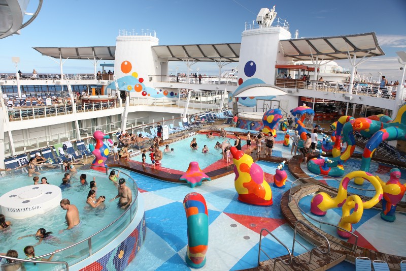 Bustling H2O Zone on the Oasis of the Seas featuring families enjoying colorful water sculptures, pools, and playful fountains under a clear blue sky.