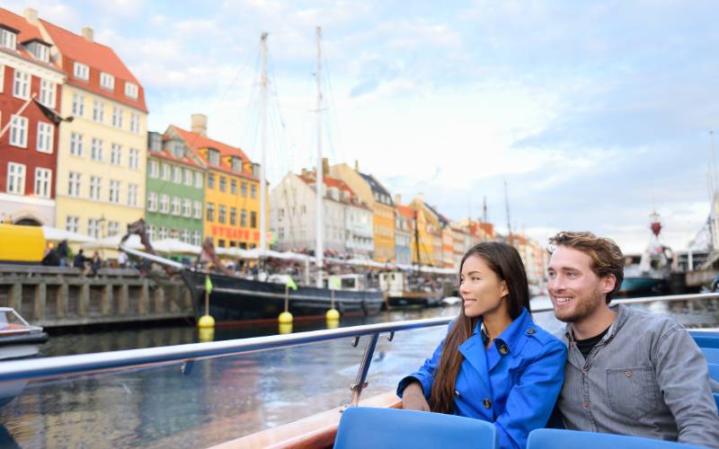 A man and a woman on an open boat tour looking at a city.