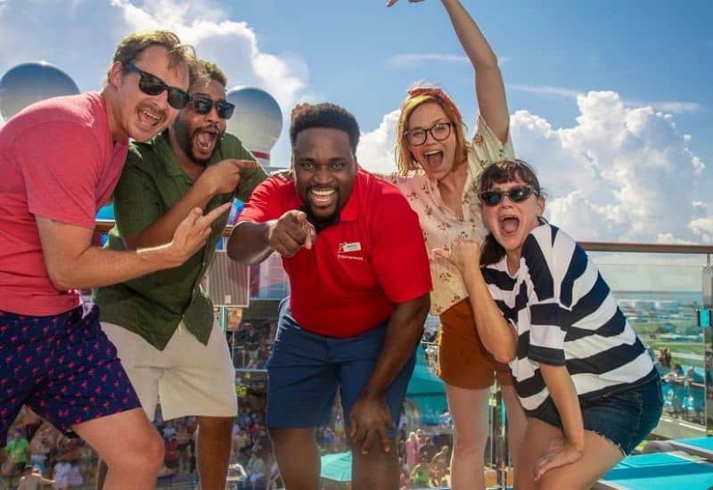 A group of excited friends posing for a photo on a sunny cruise ship deck, with a festive atmosphere and clear blue skies in the background.