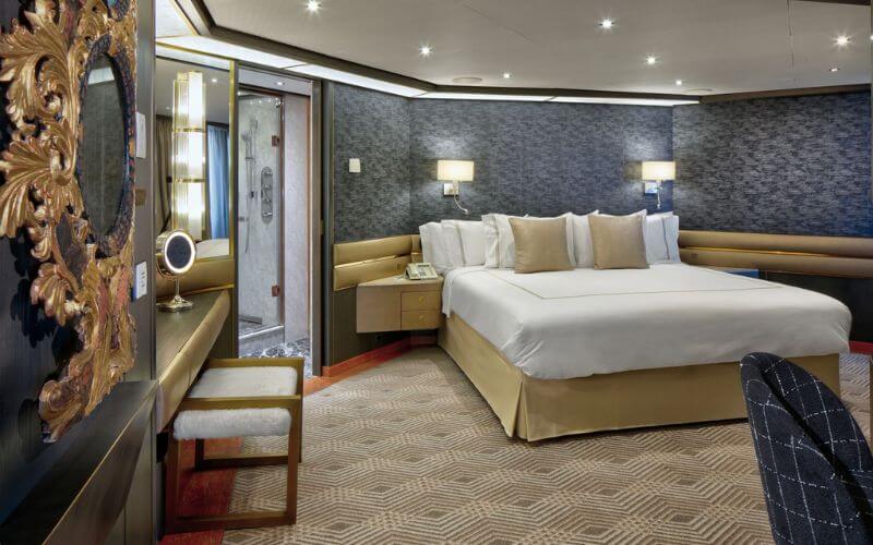 Elegant and cozy bedroom in the Pinnacle Suite on a Holland America Line cruise ship, featuring a large bed with plush bedding, tasteful decor, and ambient lighting.