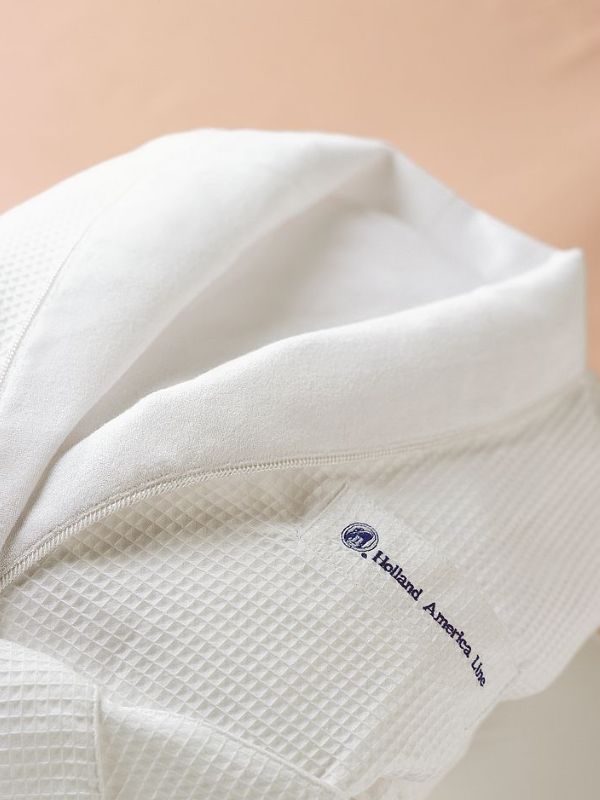 Close-up of a premium white bathrobe provided by Holland America Line, with the cruise line's logo neatly embroidered in blue, showcasing the luxurious amenities offered on board.