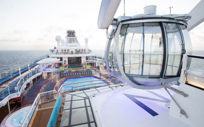 The North Star observation capsule on Royal Caribbean's Quantum of the Seas offers panoramic views from its glass-walled structure, poised high above the ship's upper deck with pools and lounges, set against the open sea horizon.