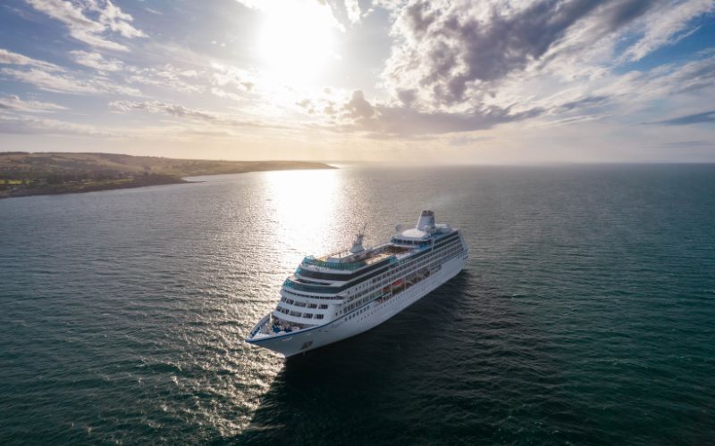 The Regatta cruise ship basking in the golden glow of the setting sun. The calm sea around the ship mirrors the sky, while the distant shores promise an array of natural wonders to explore.