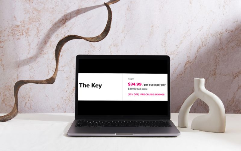 A laptop screen displaying an offer for 'The Key' on a Royal Caribbean cruise, showing a promotional price of $34.99 per guest per day, down from the full price of $49.99, advertising a 30% off pre-cruise savings. The laptop is placed on a marble table next to a modern sculptural vase, suggesting the luxury and value of the program.