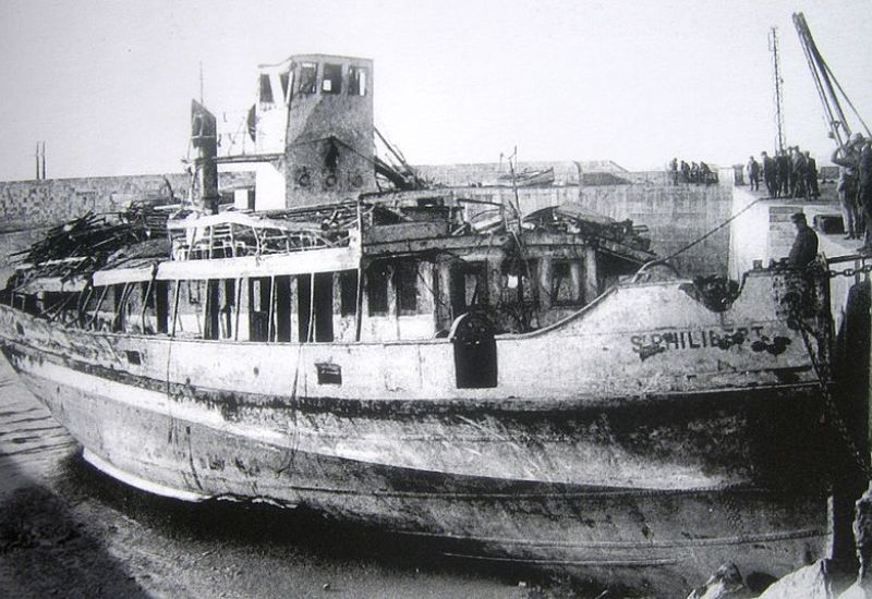 Black and white photograph of the wrecked 'Saint-Philibert' vessel, showing extensive damage and decay, as it lies beached with onlookers gathered around, capturing a moment of maritime history.