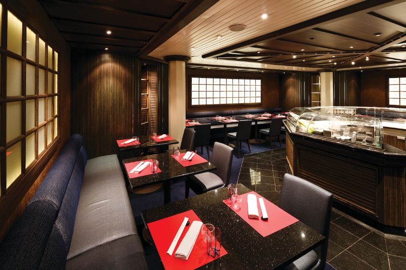 The Seishin restaurant on a Silversea cruise ship exudes a warm and inviting atmosphere with its dark wood tones, shoji screen-inspired windows, and sophisticated sushi bar, all set for a refined dining experience.