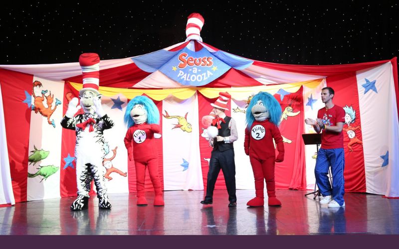 Seuss-a-Palooza Storytime and Parade on the Carnival Dream, featuring performers dressed as classic Dr. Seuss characters, including the Cat in the Hat and Thing 1 and Thing 2, entertaining guests against a whimsical Seuss-themed backdrop.