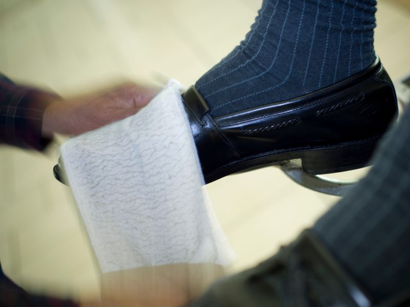 Close-up view of a person's hand buffing a shiny black dress shoe with a white towel, capturing a moment of professional shoe shining service.