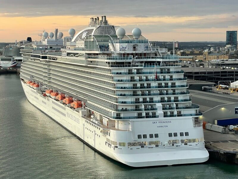 The aft view of the 'Sky Princess' cruise ship from Princess Cruises, docked at port during golden hour, with its name and home port 'Hamilton' displayed, ready to embark on another voyage.