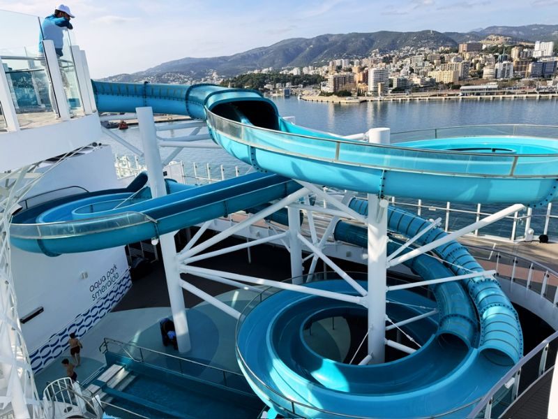 A section of a looping water slide on the Costa Smeralda cruise ship with a scenic view of a coastal cityscape in the background, illustrating the fun and adventure available on board.