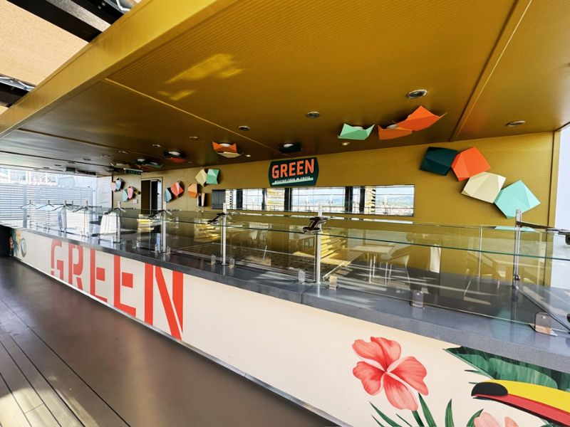 The vibrant and modern interior of the GREEN restaurant on the Costa Smeralda, with bright yellow accents and decorative geometric shapes on the walls, emphasizing a fresh and contemporary dining atmosphere.