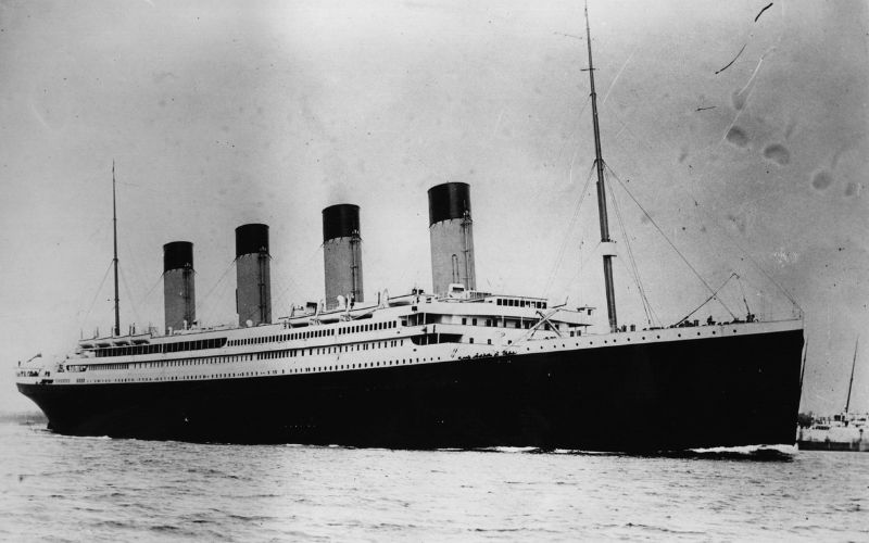 Historic black and white photo of the RMS Titanic, the iconic British passenger liner, as it sailed on its maiden voyage, with its distinctive four funnels and elegant profile.