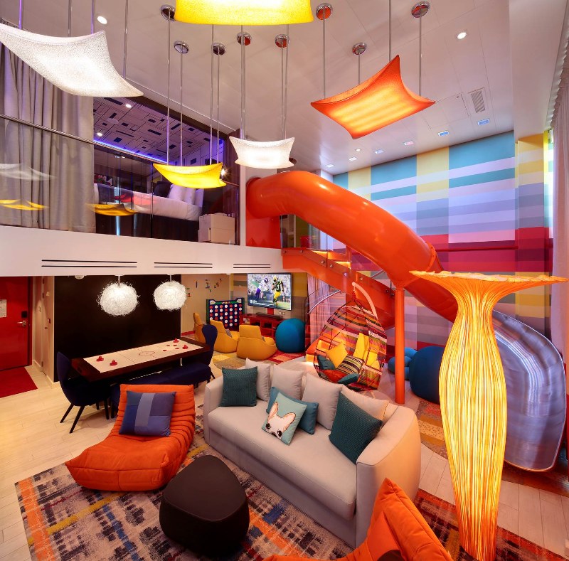 Vibrant and playful interior of the Ultimate Family Suite on 'Symphony of the Seas' featuring a slide, colourful furniture, a gaming area, and whimsical lighting.