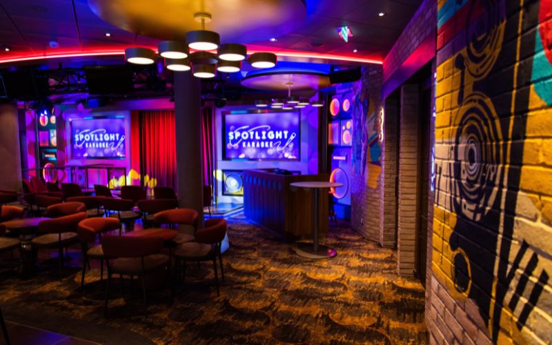 Spotlight Karaoke bar on Royal Caribbean's Wonder of the Seas, featuring a vibrant and colorful stage set for performances, surrounded by cozy seating areas with a funky and eclectic décor, ready for guests to sing their hearts out.