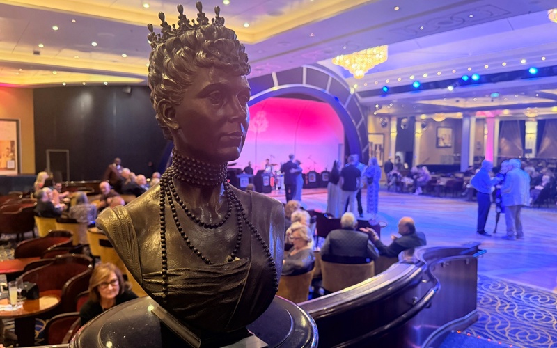 Crowned bronze bust overlooking a ballroom with people dancing and seated around the floor.