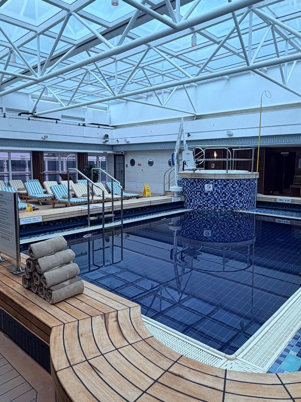 Indoor swimming pool beneath a glass roof, with loungers around the poolside.