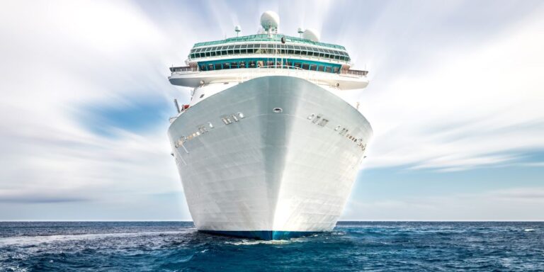 Majestic view of a cruise ship's bow as it cuts through the blue waters of the ocean under a bright, cloudy sky, showcasing the grandeur and scale of oceanic travel.