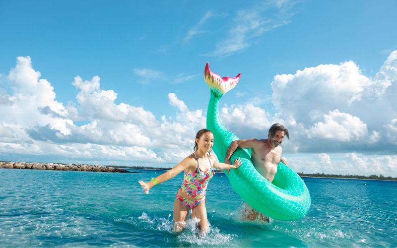 father and daughter running on the beach with whale tail floatie