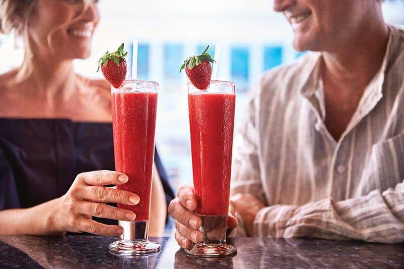 A smiling couple toasting with strawberry garnished frozen drinks, enjoying a cheerful moment together on a Princess cruise ship.