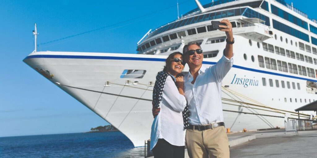 a couple taking a photo on their phone in front of an Oceania cruise ship