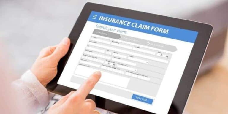 Close-up of a person's hands filling out an 'Insurance Claim Form' on a tablet, with fields for policy number, date of loss, cause of loss, and amount claimed visible on the screen.