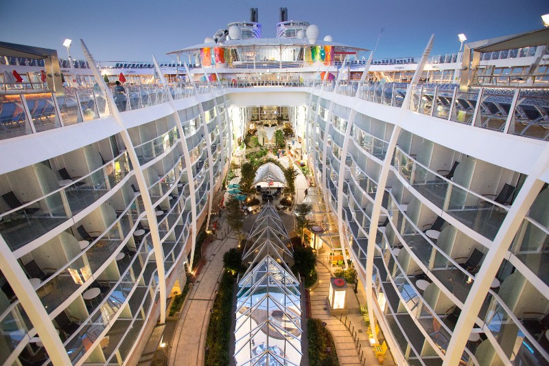 Twilight view inside the 'Symphony of the Seas' showing the internal balcony staterooms overlooking the central park area with lush greenery and walkways.