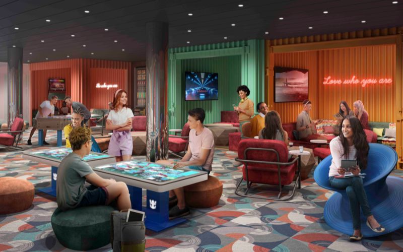 A vibrant social lounge filled with teenagers engaging in various activities, including playing foosball, using interactive digital tables, and relaxing on modern, colorful furniture. The room features neon signs with motivational phrases like "Love who you are," creating a lively and welcoming atmosphere. The decor is eclectic, with a mix of industrial and contemporary elements, promoting a fun and inclusive environment.