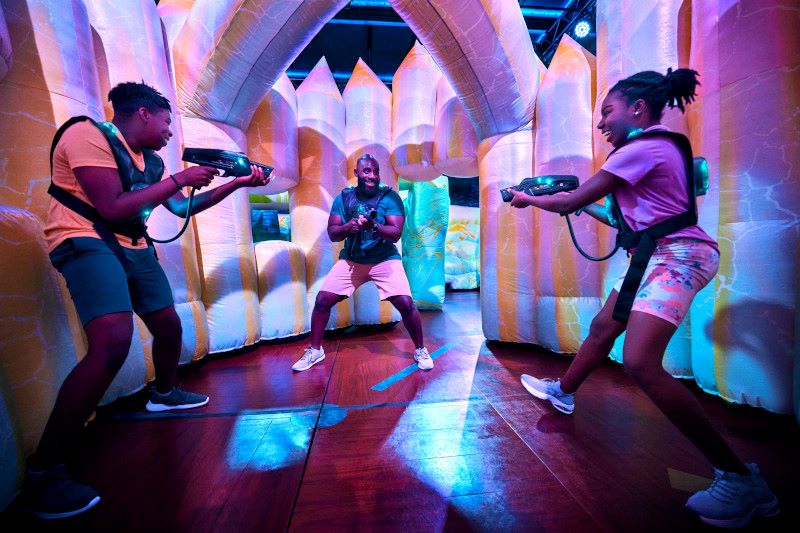 Amidst vibrant neon colors and an inflatable arena, a family is fully engaged in a lively laser tag match on Royal Caribbean's Freedom of the Seas. The excitement and action-packed fun of the game illuminate their faces, offering a glimpse into the ship's thrilling and interactive entertainment options.