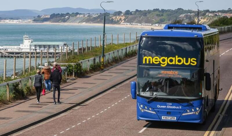 A Megabus coach travlling along a seaside road.