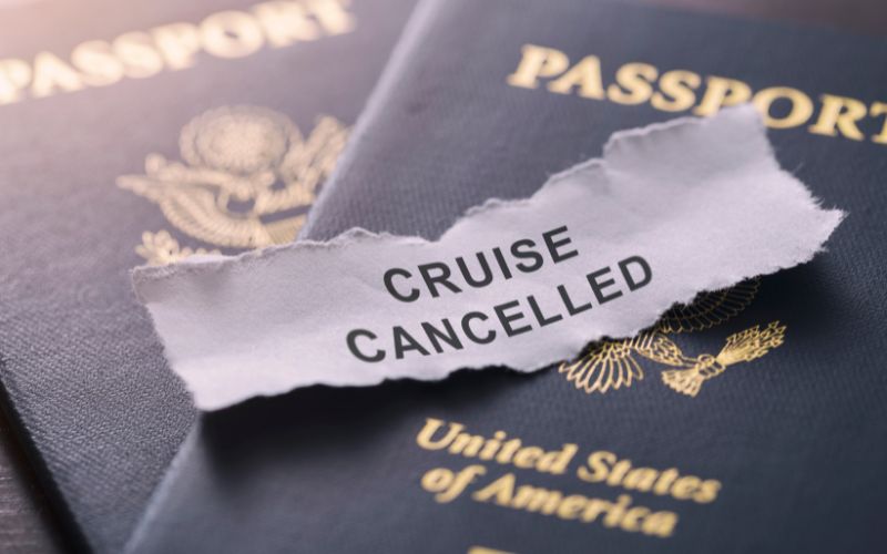 Torn piece of paper with the text 'CRUISE CANCELLED' placed on top of two United States passports, indicating a disrupted travel plan.