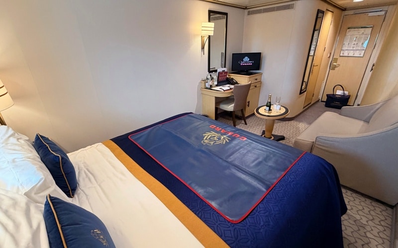 View across the double bed towards the sofa, desk and entrance in a Queen Mary 2 cabin.