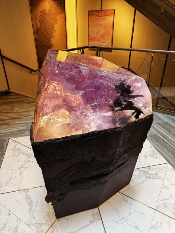 A striking sculpture displayed aboard the Seabourn Venture, beautifully crafted from recycled plastic. The artwork is a large, faceted piece, resembling a gemstone with rich purple and pink hues set in a rugged black base. The sculpture not only serves as an eye-catching centerpiece but also emphasizes the ship's commitment to environmental awareness and sustainability. Its placement in a well-lit area with artistic backdrops enhances its visual impact and draws attention to its intricate details.