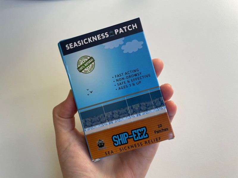A hand holding a box of seasickness patches labeled "SHIP-EEZ" for sea sickness relief. The box indicates that the patches are fast-acting, non-drowsy, safe and effective, and suitable for ages 3 and up. The packaging design features a maritime theme with a blue sky, clouds, and ocean waves.