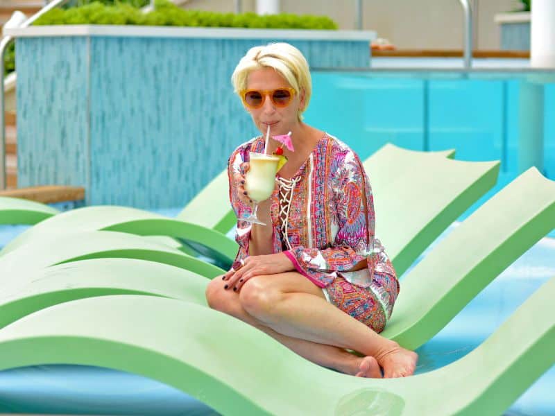 A woman enjoying a solo cruise vacation, relaxing on a sun lounger with a piña colada, by the ship's poolside.