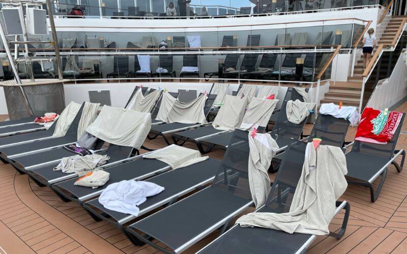 Sun loungers on a cruise ship deck are reserved with towels and personal items, awaiting the return of passengers who've marked their spots for relaxation and sunbathing, reflecting a common practice on busy sea days.