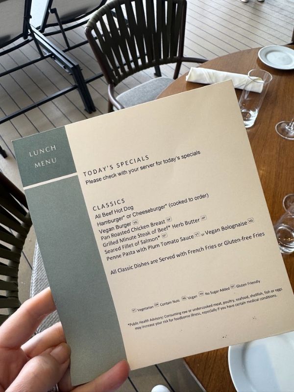 The lunch menu showcases a variety of dining options available on the Seabourn Venture, catering to diverse tastes and dietary preferences. Today's specials are highlighted at the top, suggesting daily variations, with a section below dedicated to "Classics." The classics include all-beef hot dogs, cheeseburgers (available as a cooked-to-order option), hamburgers, vegan roasted chicken breast, pan-fried minute steak of beef with herb butter, grilled fillet of salmon, and penne pasta with plum tomato sauce and vegan Bolognese. The menu notes that all classic dishes are served with French fries or gluten-free fries, accommodating different dietary needs with symbols indicating vegetarian, vegan, no sugar added, and gluten-free options.